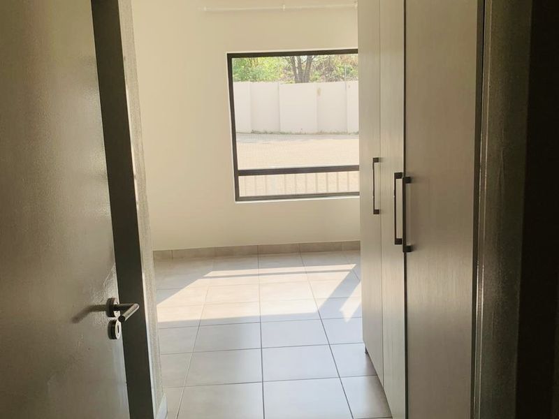 A bright, empty bedroom featuring neutral tiled flooring and ample built-in cupboard storage, offering a clean and versatile space.
