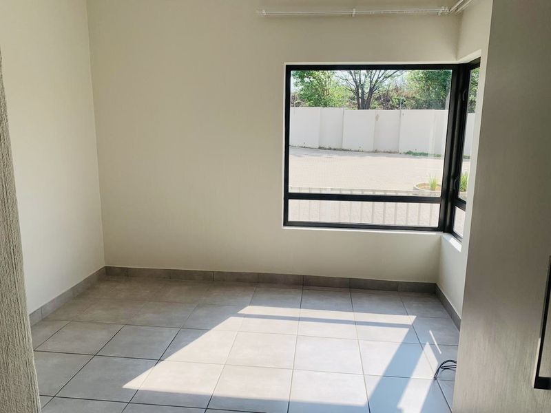 A bright, empty bedroom featuring neutral tiled flooring and a large aluminium-framed window providing natural light.