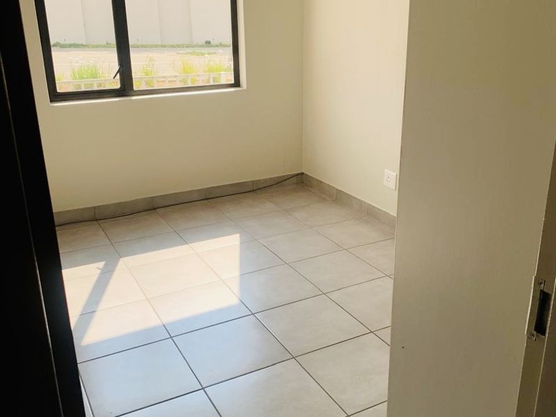 A bright, empty bedroom featuring neutral tiled flooring and a modern aluminium-framed window, offering a clean and versatile space ready for personalization.