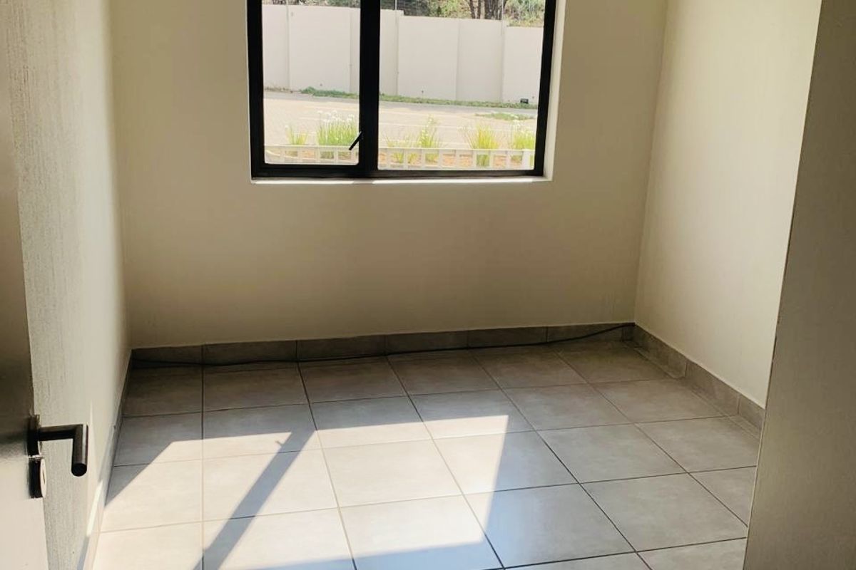 A clean, empty bedroom featuring neutral tiled flooring and a modern aluminium window frame, providing a blank canvas for interior design.