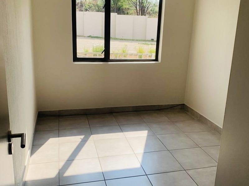 A clean, empty bedroom featuring neutral tiled flooring and a modern aluminium window frame, providing a blank canvas for interior design.