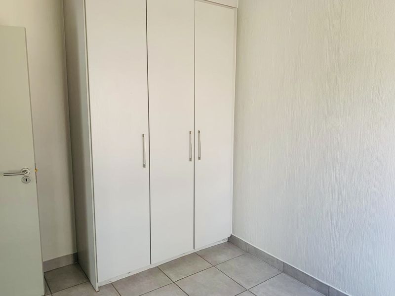 A clean, empty bedroom featuring neutral tiled flooring and a functional built-in wardrobe with modern handles.
