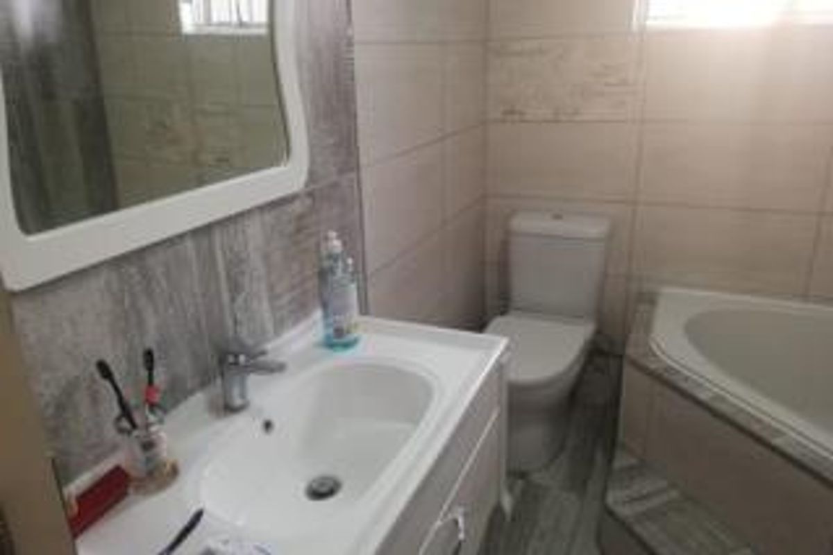 A functional bathroom featuring a vanity cabinet with a basin, a corner bathtub, a toilet, and neutral wall and floor tiling.