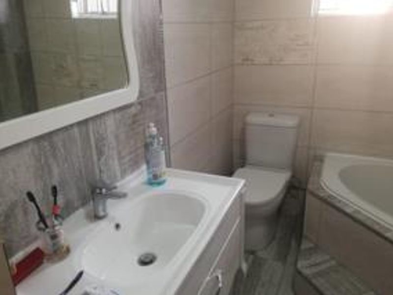 A functional bathroom featuring a vanity cabinet with a basin, a corner bathtub, a toilet, and neutral wall and floor tiling.
