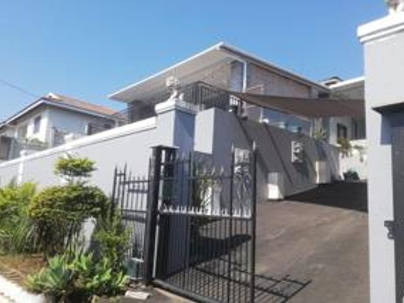 Front elevation of the property featuring a secure gated entrance, paved driveway, and an elevated balcony area with shade sail.