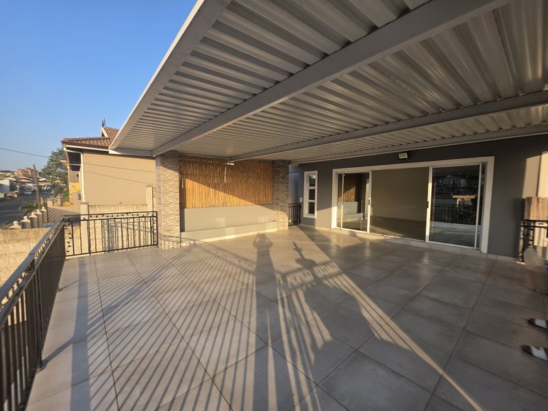 A spacious covered patio featuring tiled flooring, a corrugated metal roof, and a stone-clad feature wall, providing seamless access to the interior living space.
