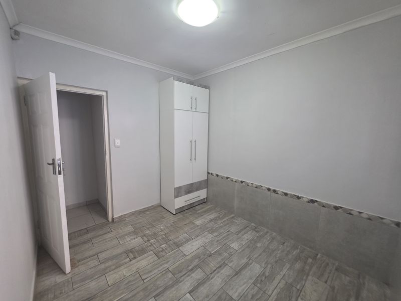 A clean, empty bedroom featuring modern wood-look tiled flooring, partial wall tiling, and a built-in wardrobe.