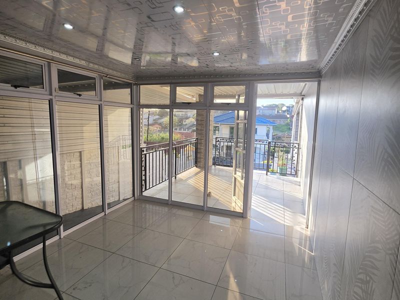 A bright, enclosed balcony or sunroom featuring tiled floors, decorative ceiling panels, and large aluminium sliding doors leading to an outdoor area.