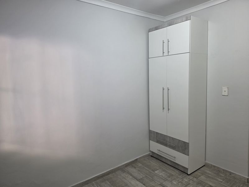 A clean, minimalist bedroom featuring modern tiled flooring and a built-in wardrobe with contemporary finishes.