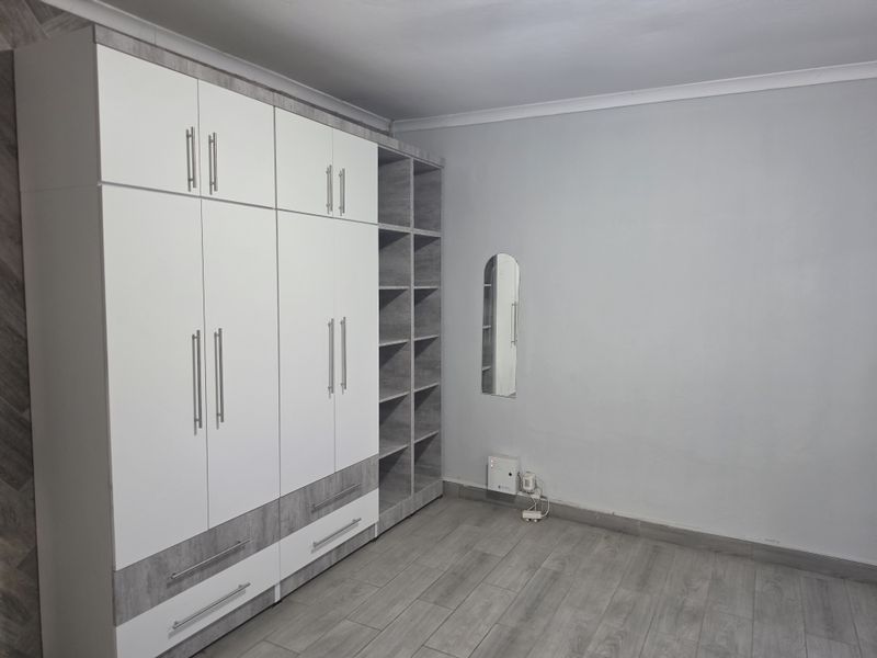 A clean, empty bedroom featuring modern built-in cupboards with a mix of white and grey wood-grain finishes and matching laminate flooring.