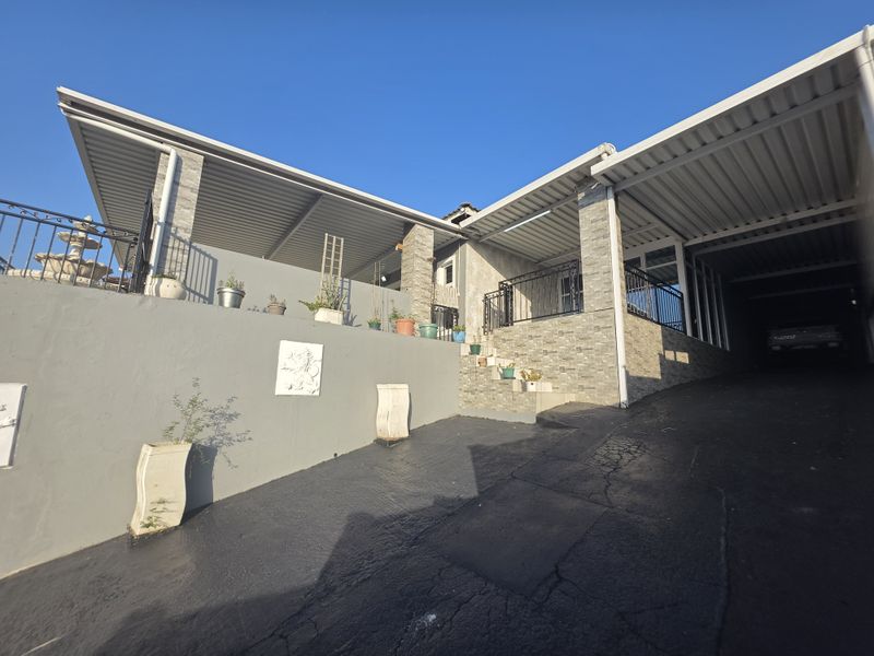 Front exterior view featuring a covered driveway, stone-clad retaining wall, and concrete stairs leading to the entrance.