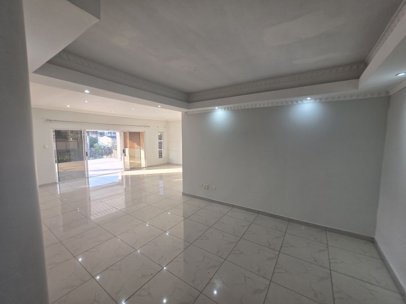 Spacious, empty living area featuring polished porcelain floor tiles, recessed ceiling lighting, decorative cornices, and large sliding glass doors leading to an outdoor space.