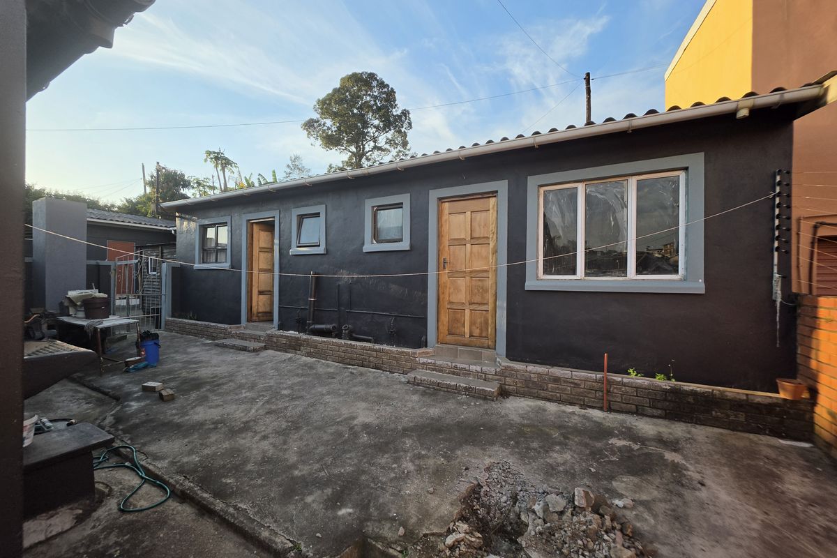 Rear exterior view of the townhouse featuring a concrete patio area, dark painted walls, timber door, and aluminium window frames.