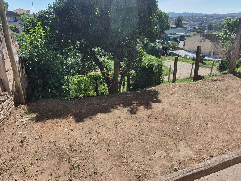 A rear outdoor area featuring a concrete block retaining wall, wire fencing, and an unlandscaped yard with potential for garden development.
