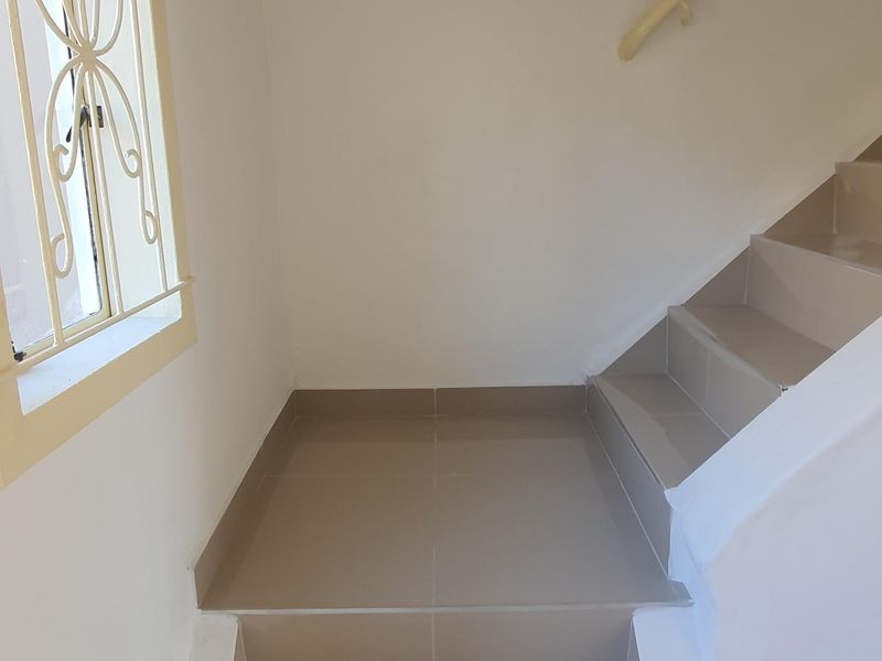A clean, tiled staircase area featuring a security window grille and a wall-mounted handrail, providing access between levels.