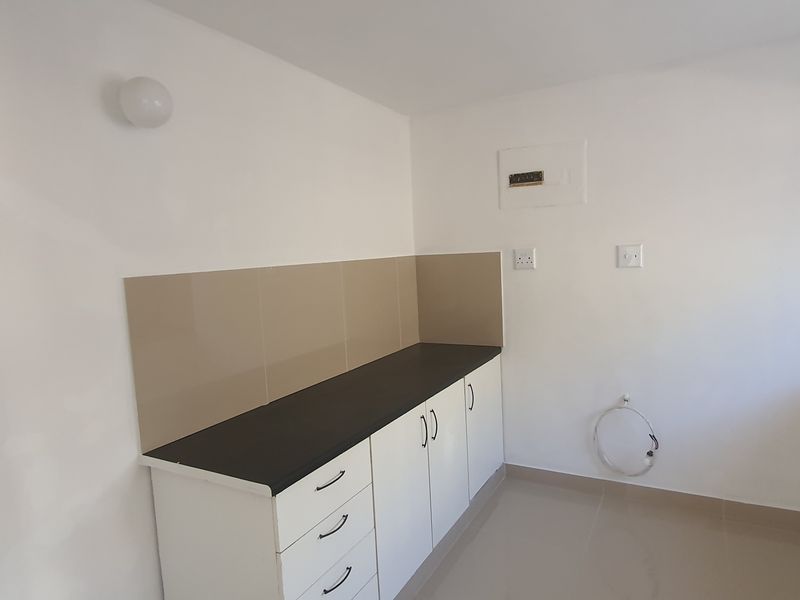 A clean, empty kitchen area featuring white built-in cabinetry, dark laminate countertops, and neutral tiled splashbacks, ready for appliance installation.