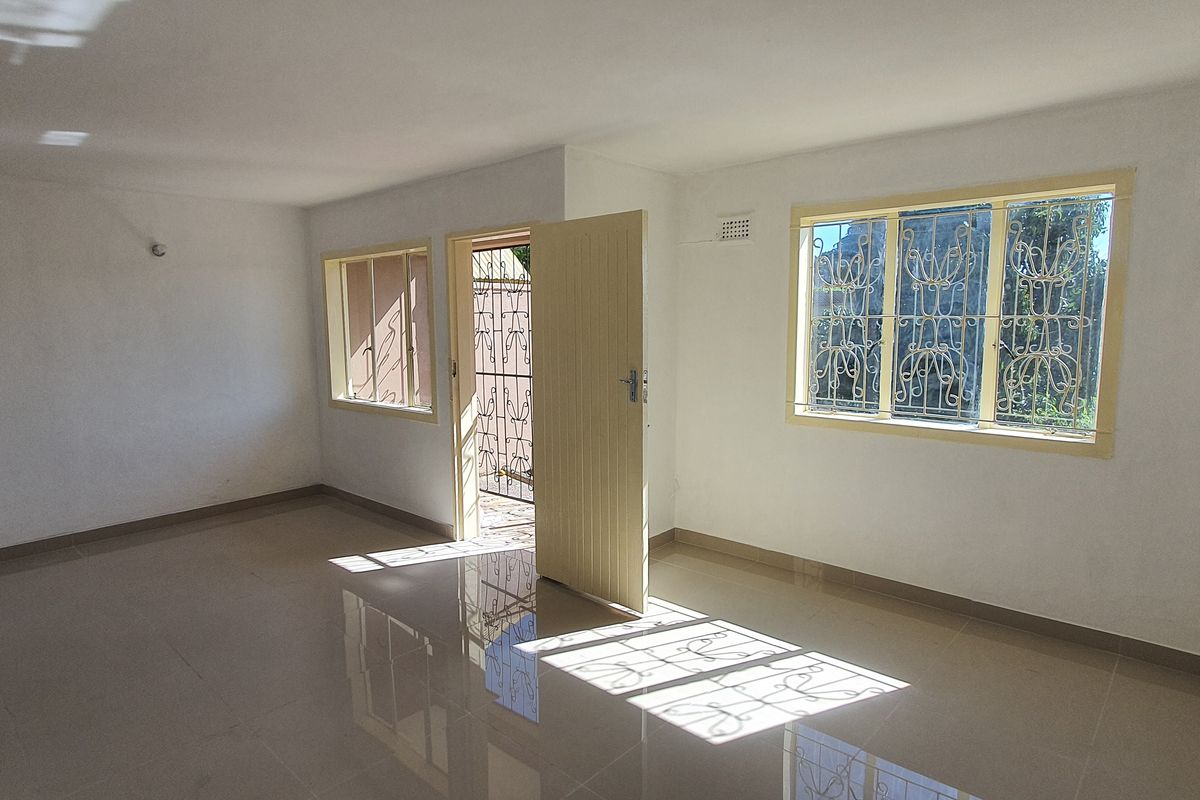 A bright, empty living area featuring tiled flooring, security bars on windows, and a secure entrance door.