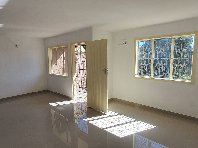 A bright, empty living area featuring tiled flooring, security bars on windows, and a secure entrance door.