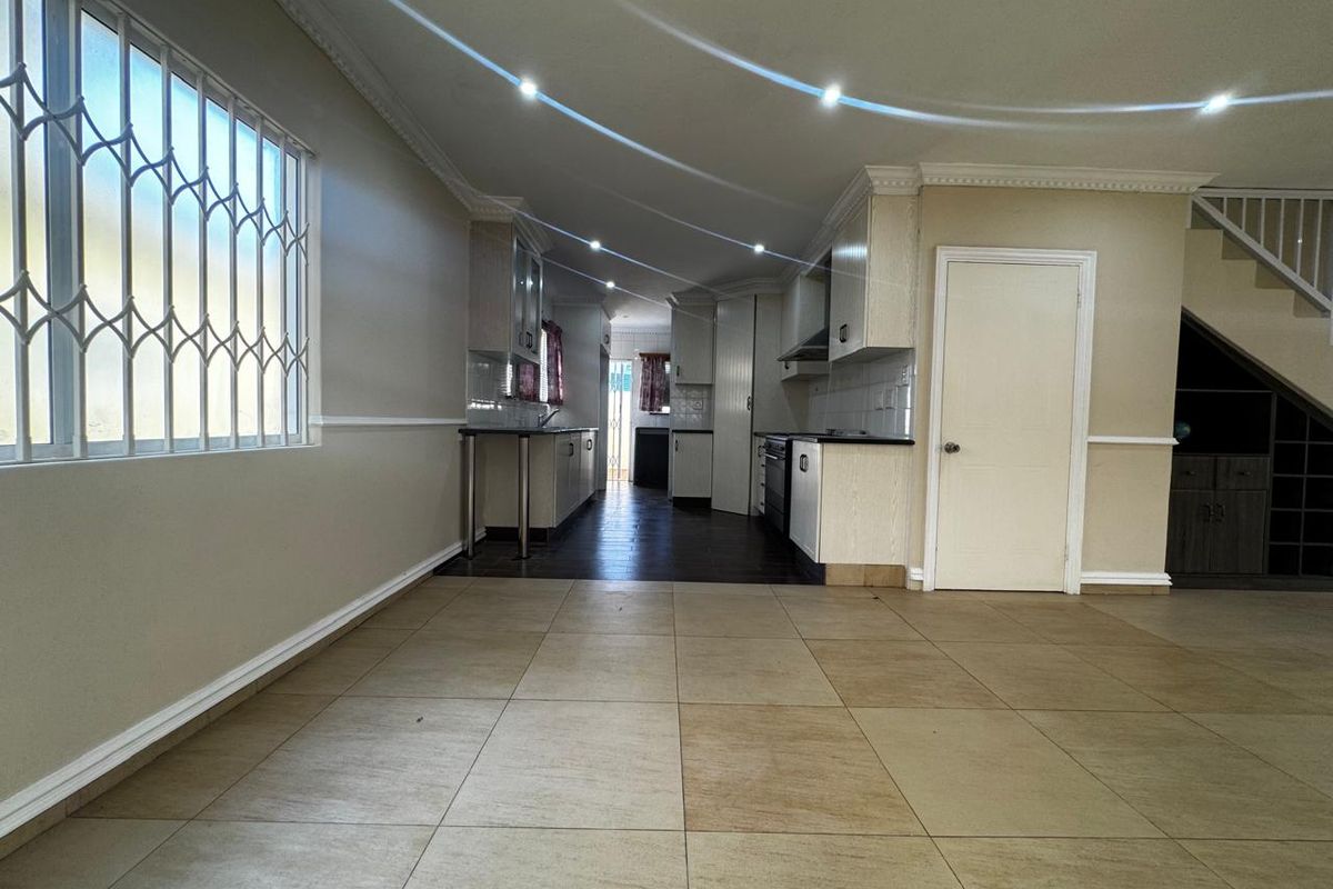 An open-plan kitchen area featuring tiled flooring, built-in cabinetry, and recessed lighting, with a staircase visible in the background.