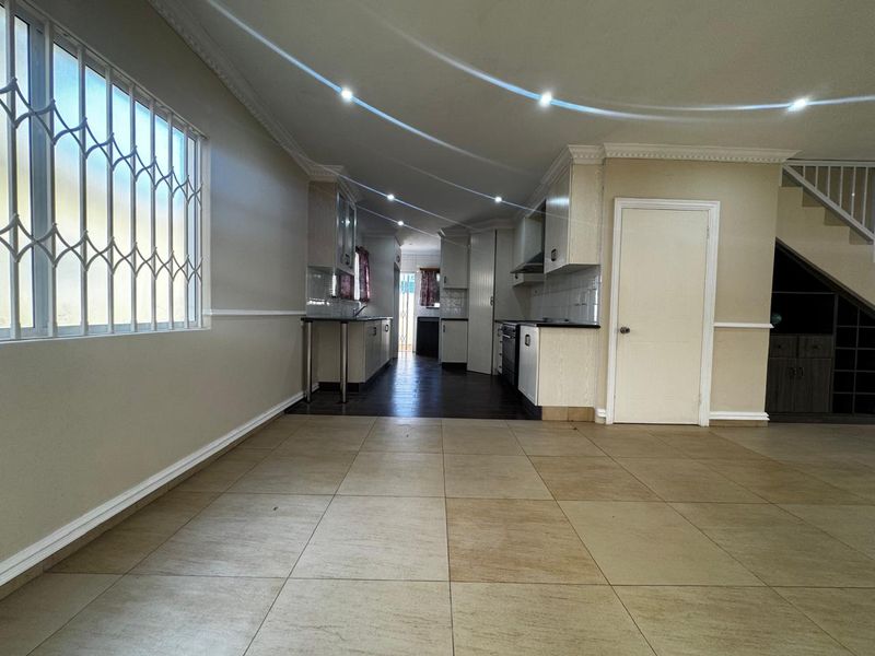 An open-plan kitchen area featuring tiled flooring, built-in cabinetry, and recessed lighting, with a staircase visible in the background.