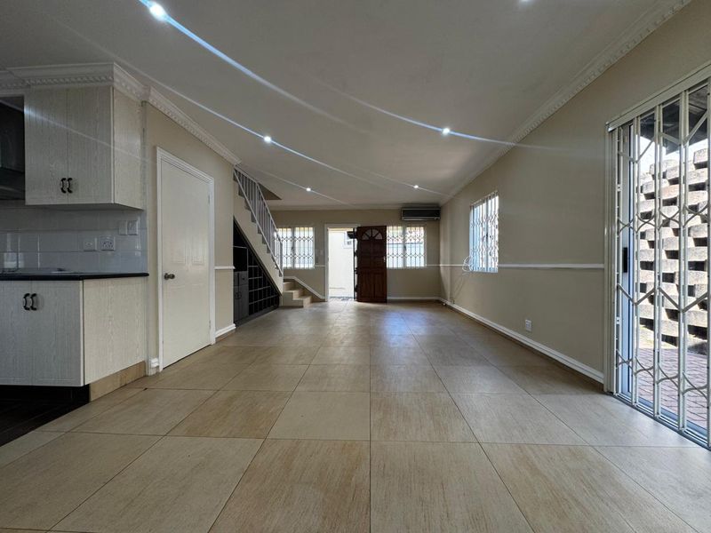 Spacious open-plan living area featuring tiled floors, recessed lighting, built-in staircase storage, and direct access to the exterior through security-fitted doors.
