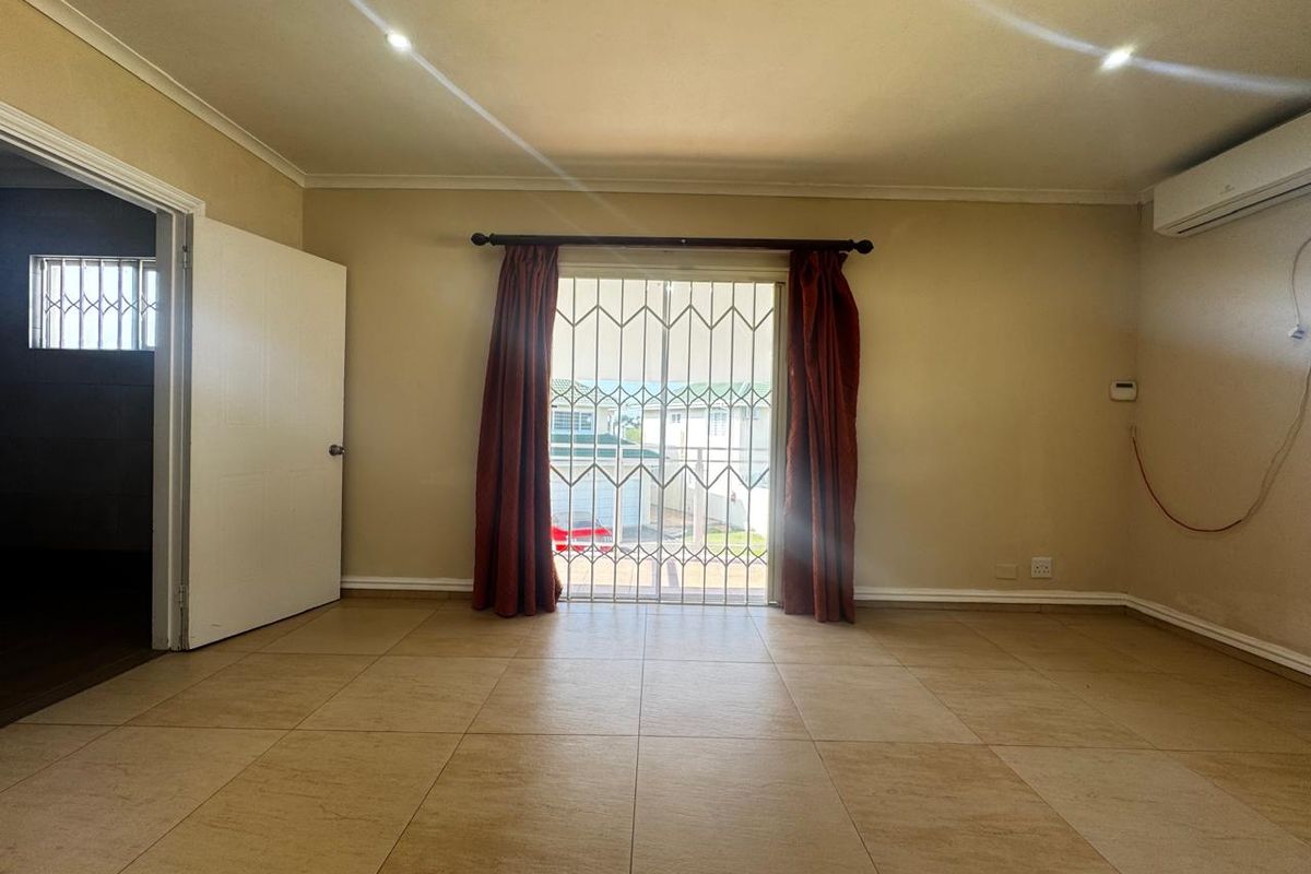 An empty living room featuring tiled flooring, recessed downlights, a wall-mounted air conditioner, and a sliding glass door with a security gate.