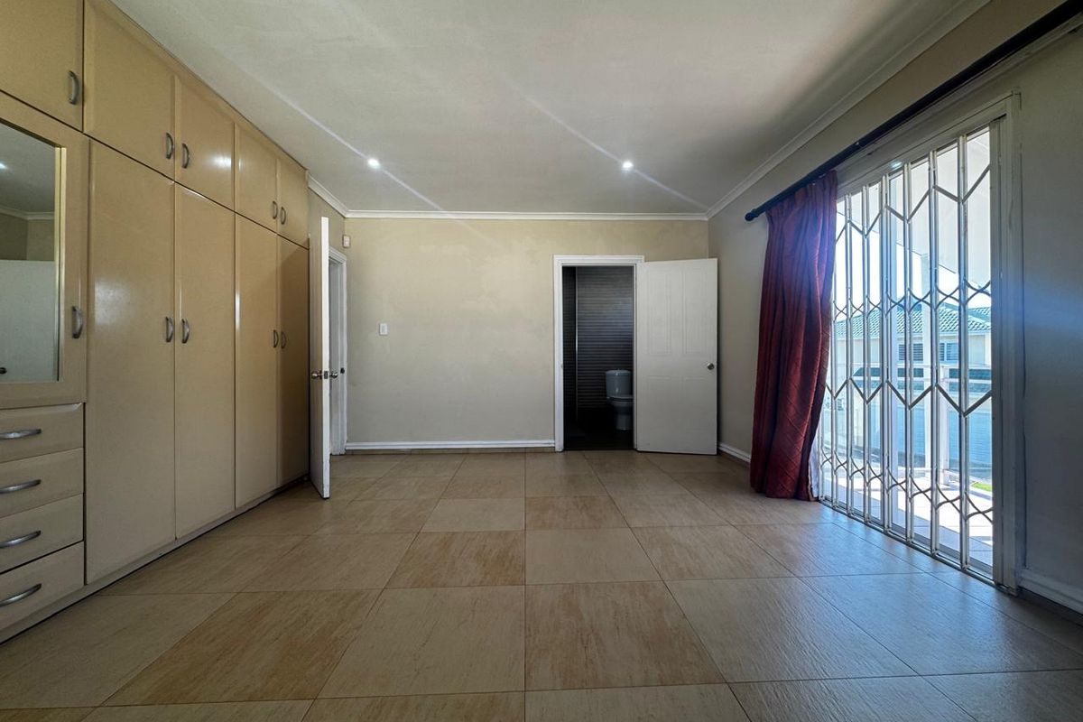 Spacious bedroom featuring built-in cupboards, tiled flooring, and direct access to an en-suite bathroom, with a security gate leading to an outdoor area.