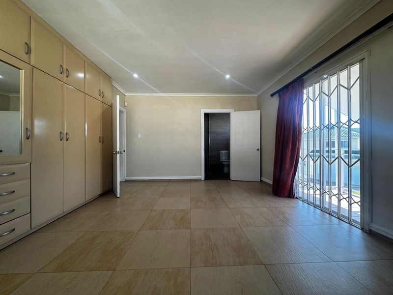 Spacious bedroom featuring built-in cupboards, tiled flooring, and direct access to an en-suite bathroom, with a security gate leading to an outdoor area.