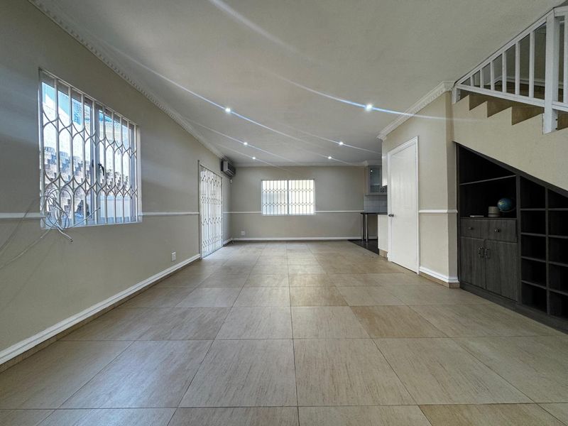 Spacious open-plan living area featuring neutral tiled flooring, recessed lighting, crown molding, and convenient built-in under-stair storage cabinetry.