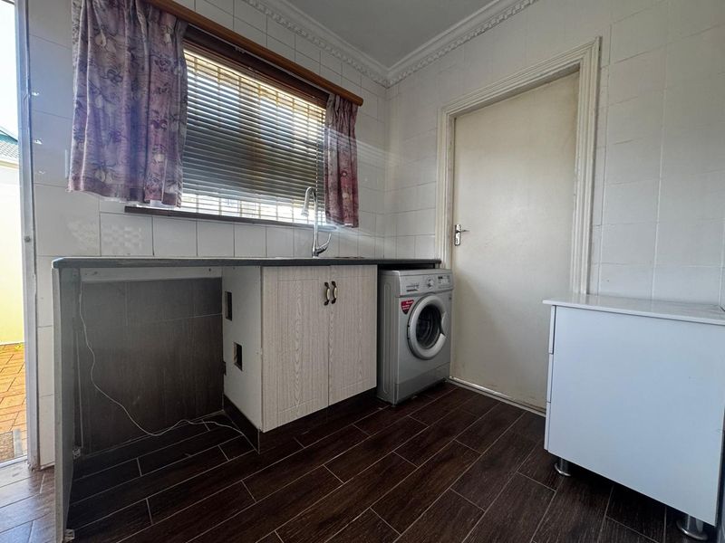 A functional laundry room featuring tiled walls, dark wood-look flooring, built-in cabinetry with a sink, and space for a washing machine.