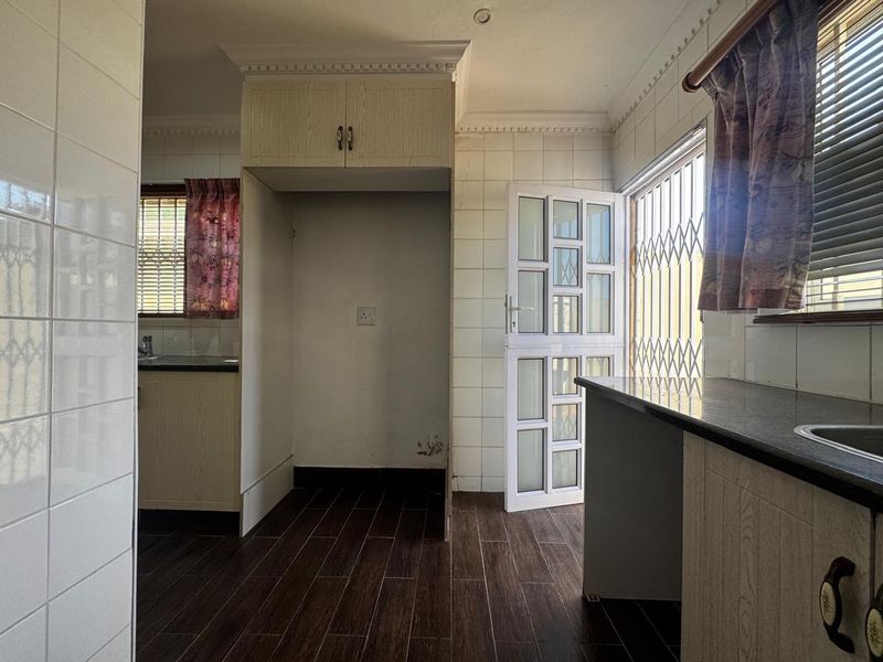 A functional kitchen featuring tiled walls, dark wood-look floor tiles, granite countertops, and built-in cabinetry with a dedicated space for a refrigerator.