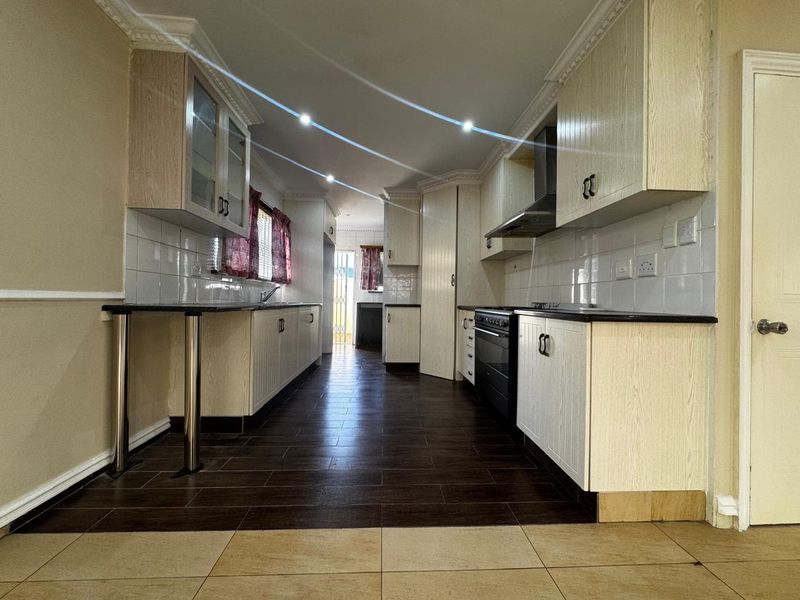 A spacious kitchen featuring light-toned cabinetry, dark tiled flooring, a built-in oven with extractor fan, and ample counter space.