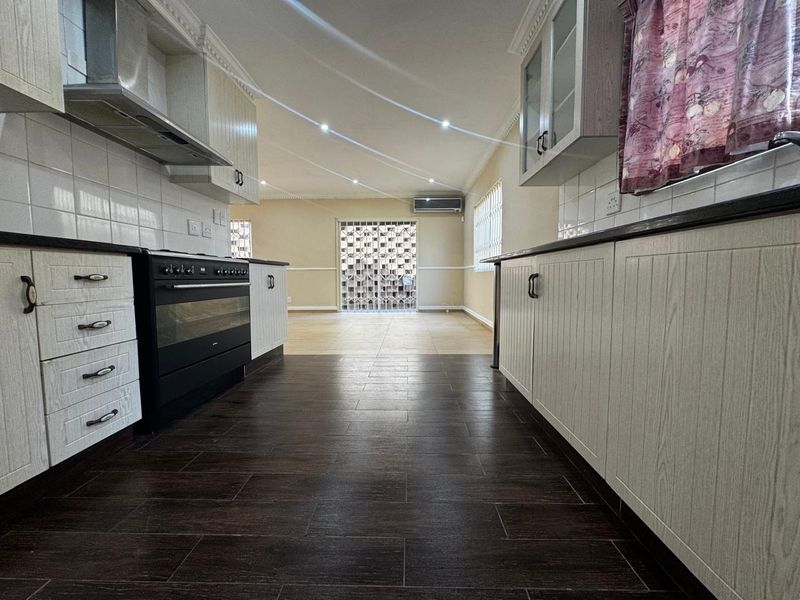 Spacious open-plan kitchen and living area featuring modern cabinetry, dark tiled flooring, and integrated lighting, leading to a secure rear entrance.