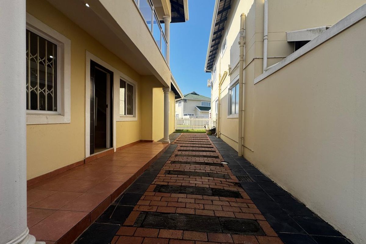 A side walkway featuring paved brick pathways, covered patio access, and exterior drainage infrastructure between two residential structures.