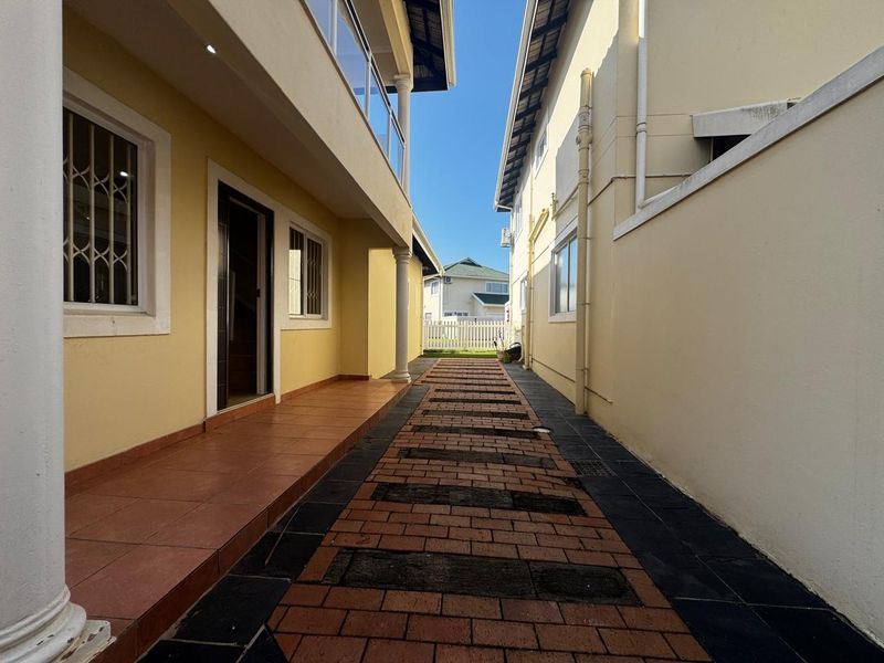 A side walkway featuring paved brick pathways, covered patio access, and exterior drainage infrastructure between two residential structures.