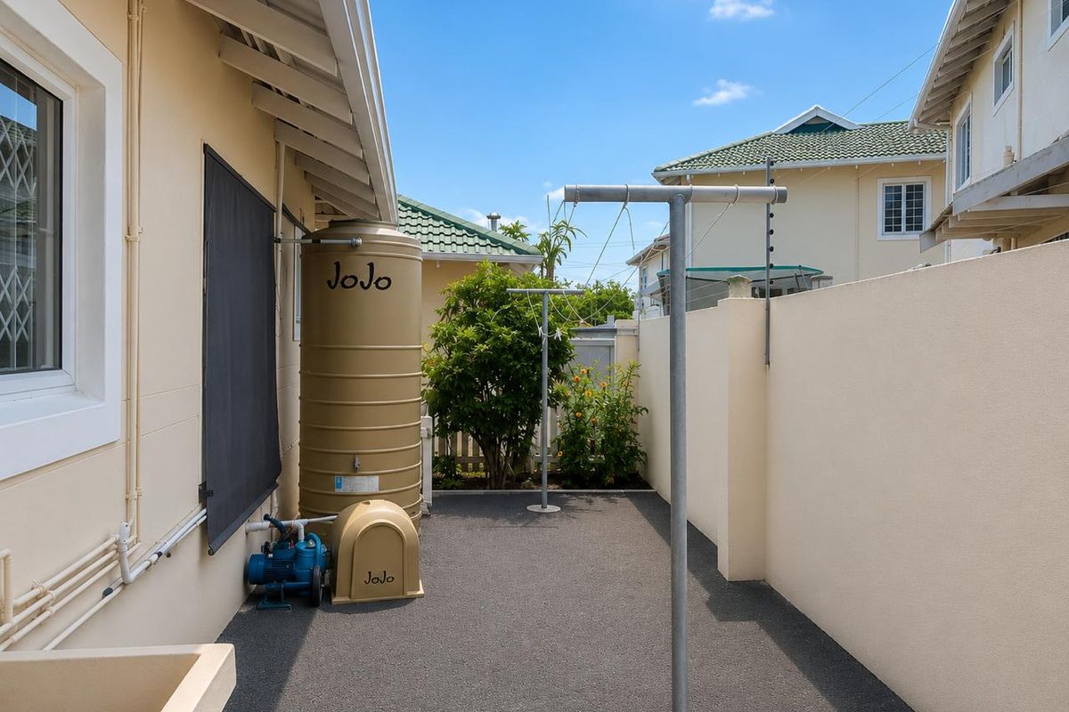 A neat and well-maintained rear courtyard featuring a water storage tank, pump system, and fixed washing lines within a secure boundary wall.