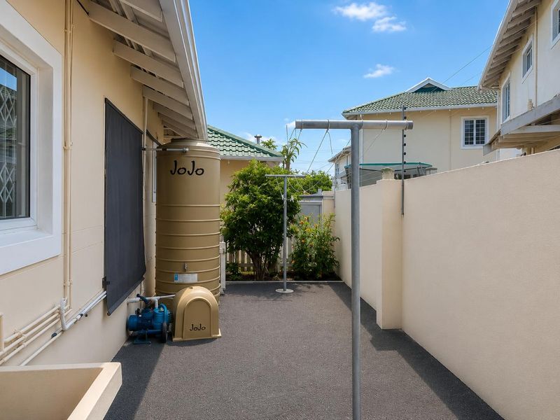 A neat and well-maintained rear courtyard featuring a water storage tank, pump system, and fixed washing lines within a secure boundary wall.