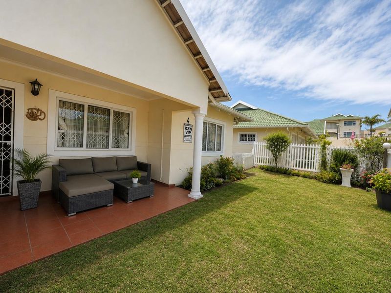 A well-maintained covered patio featuring tiled flooring and a decorative column, overlooking a neat private garden with a white picket fence.