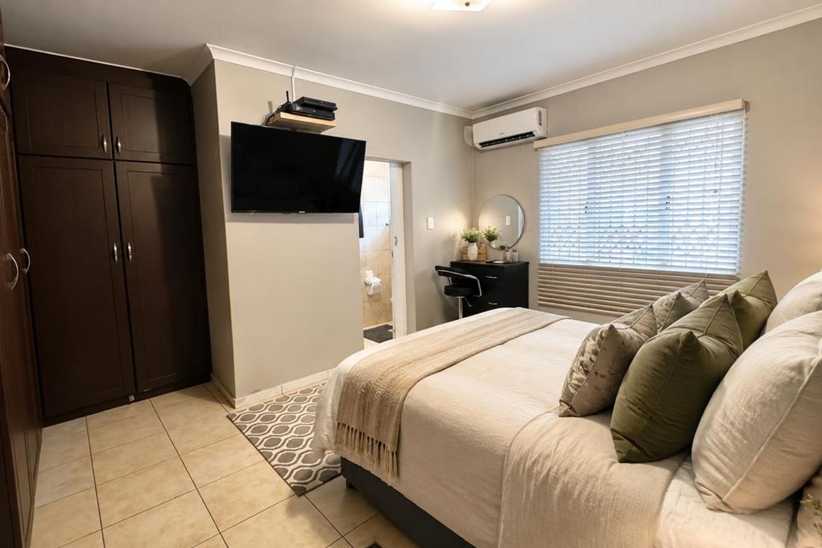 A well-maintained bedroom featuring built-in cupboards, tiled flooring, an air conditioning unit, and venetian blinds, with an en-suite bathroom access.