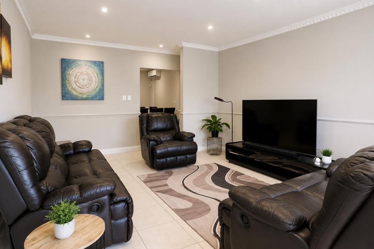 A well-maintained living room featuring tiled flooring, crown molding, chair rail detailing, and recessed downlighting, with a view into an adjacent air-conditioned space.