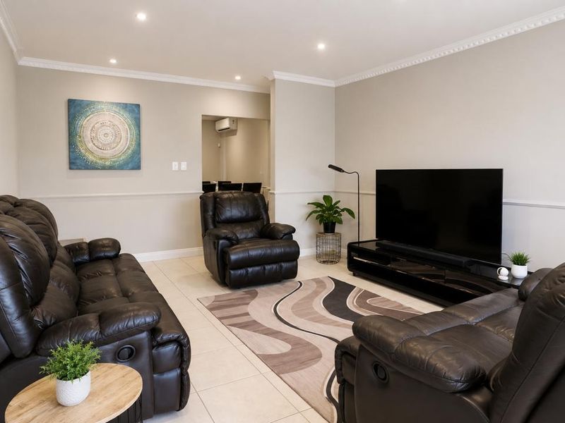 A well-maintained living room featuring tiled flooring, crown molding, chair rail detailing, and recessed downlighting, with a view into an adjacent air-conditioned space.