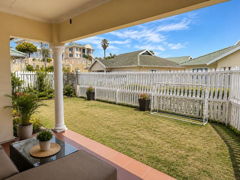 A covered patio area featuring tiled flooring and a support column, overlooking a private garden enclosed by a white picket fence.