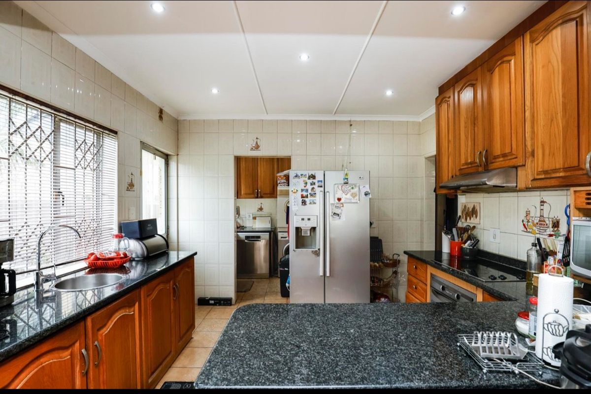 Functional kitchen featuring granite countertops, wooden cabinetry, built-in oven, extractor fan, and tiled splashbacks with an adjacent scullery area.