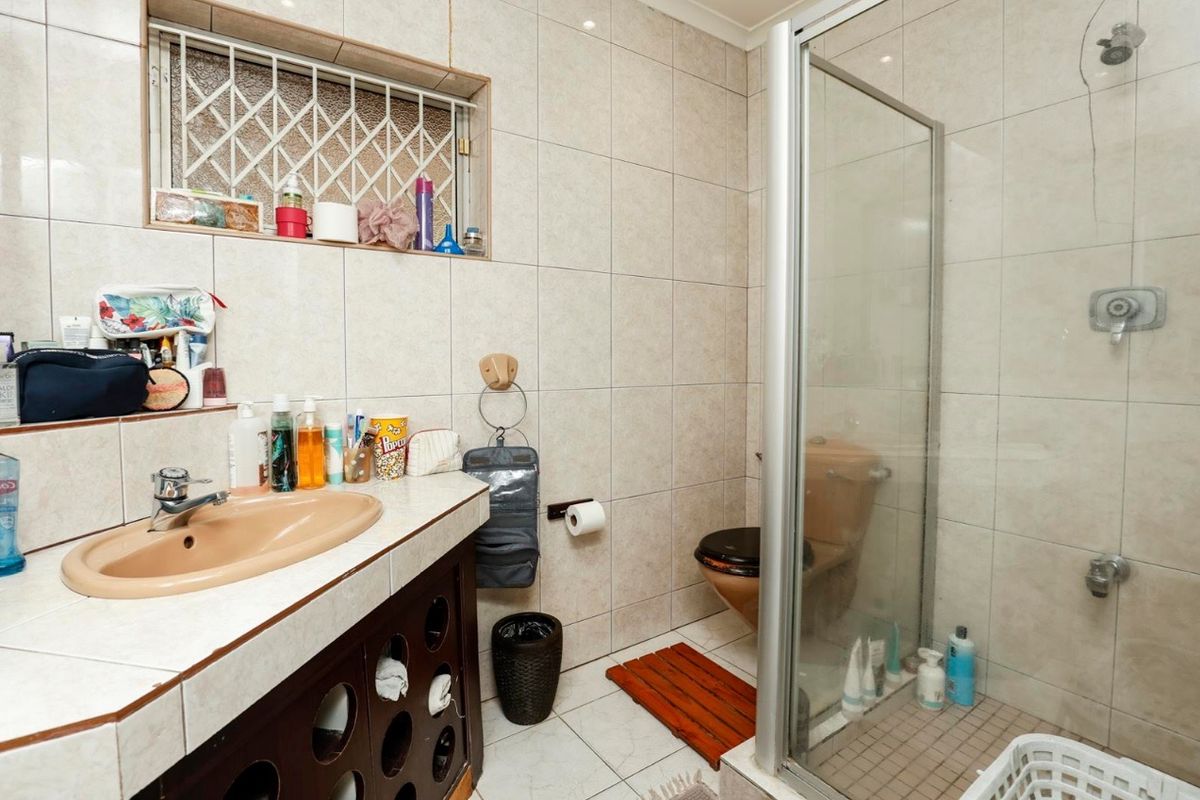 A functional bathroom featuring a tiled shower enclosure, vanity basin, and toilet, with neutral wall and floor tiling throughout.