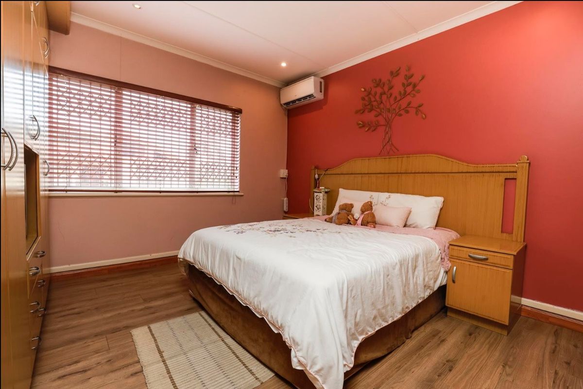A bedroom featuring laminate flooring, built-in cupboards, an air conditioning unit, and venetian blinds.