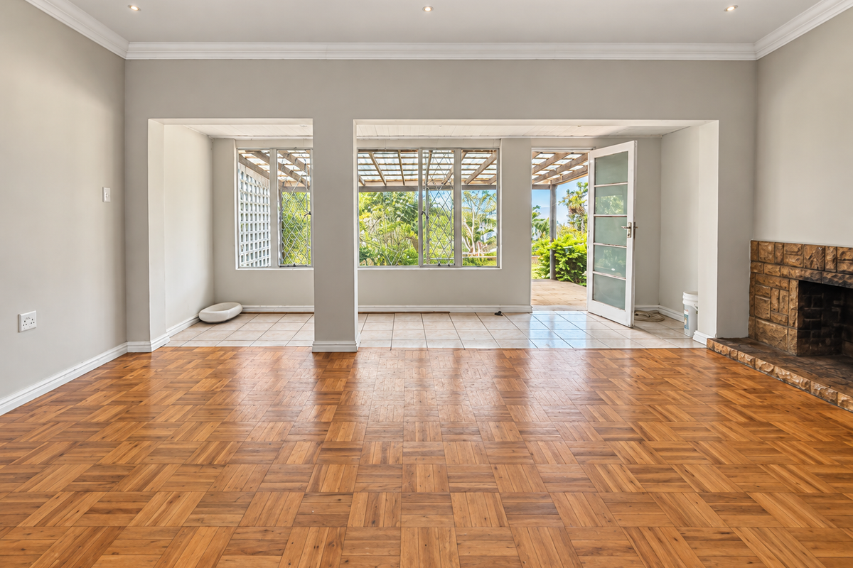 Spacious living room featuring classic parquet flooring, a stone fireplace, and direct access to a covered patio through a glass door.