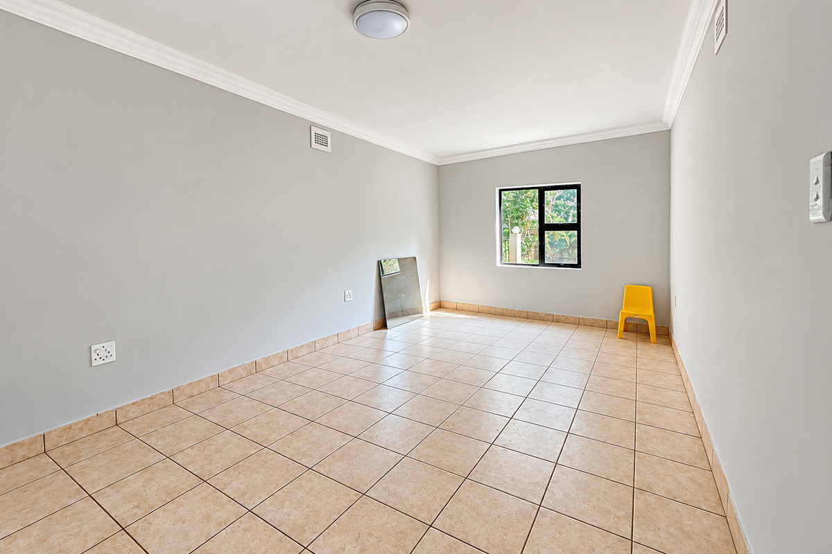 A clean, empty bedroom featuring neutral wall paint, durable tiled flooring, and a window providing natural light.