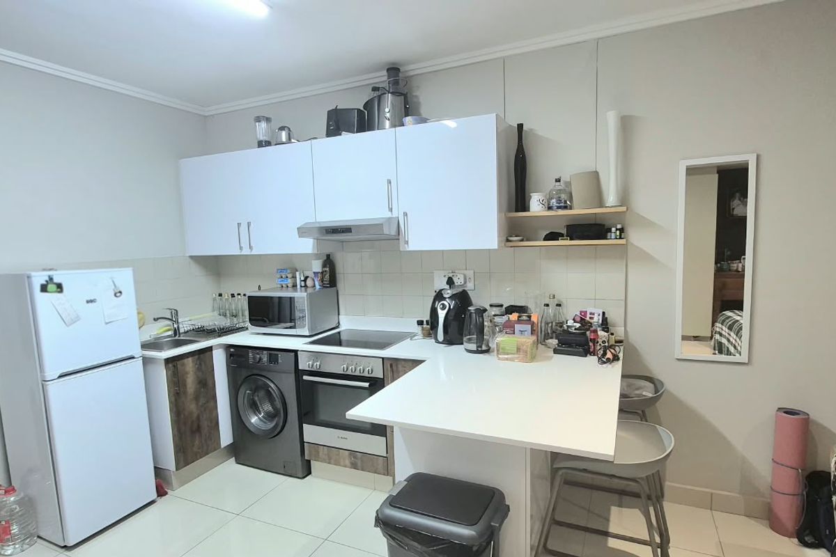 Compact kitchen featuring white upper cabinetry, integrated oven and hob, breakfast counter, and tiled flooring in an open-plan layout.