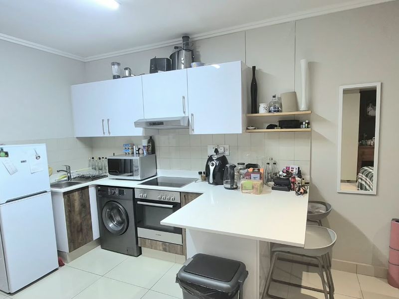 Compact kitchen featuring white upper cabinetry, integrated oven and hob, breakfast counter, and tiled flooring in an open-plan layout.