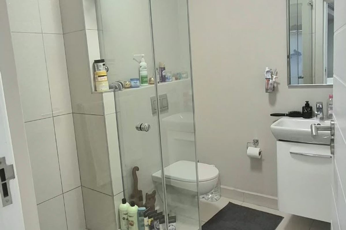 Modern bathroom featuring a glass-enclosed shower, wall-mounted toilet, and a sleek vanity basin with neutral floor and wall tiling.